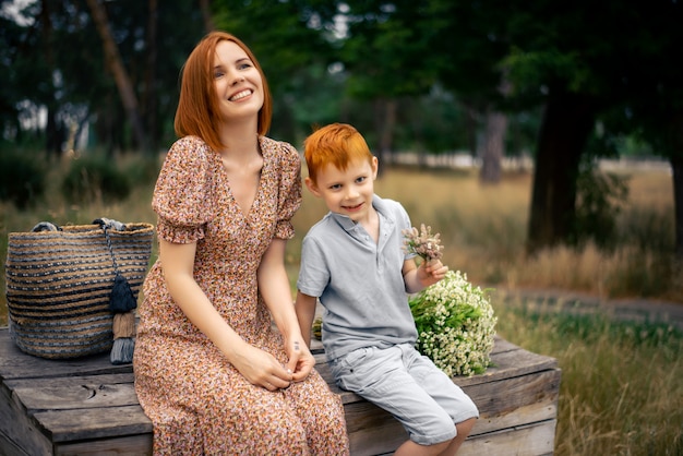 Madre e hijo con cabello rojo con un gran ramo de flores silvestres en la naturaleza en verano