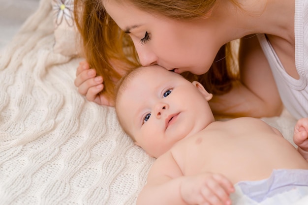 Madre e hijo en una cama blanca mamá y niña en pañales jugando en dormitorio soleado