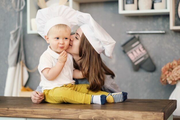 Foto madre e hijo en la cocina, sombreros blancos de chef, madre besa a su hijo, relaciones de madre e hijo