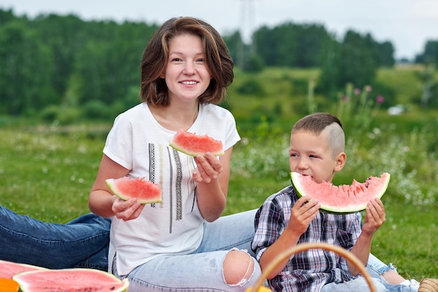 Madre e hijo comiendo sandía en el prado o el parque Familia feliz en retrato al aire libre de picnic