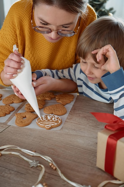 Madre e hijo decorando juntos galletas de jengibre navideñas con azúcar glas