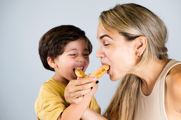 Madre e hijo disfrutando y comiendo un bocadillo latinoamericano llamado tequenos expresiones divertidas en sus rostros