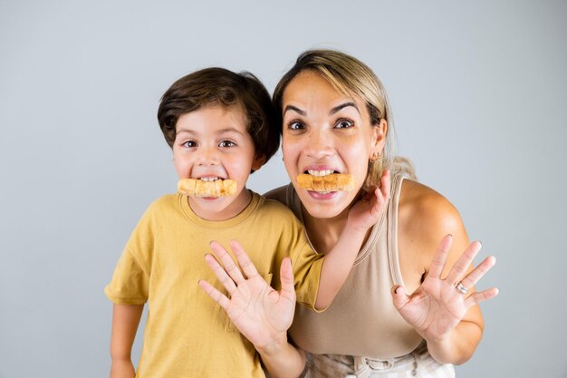 Madre e hijo disfrutando y comiendo un bocadillo latinoamericano llamado tequenos expresiones divertidas en sus rostros