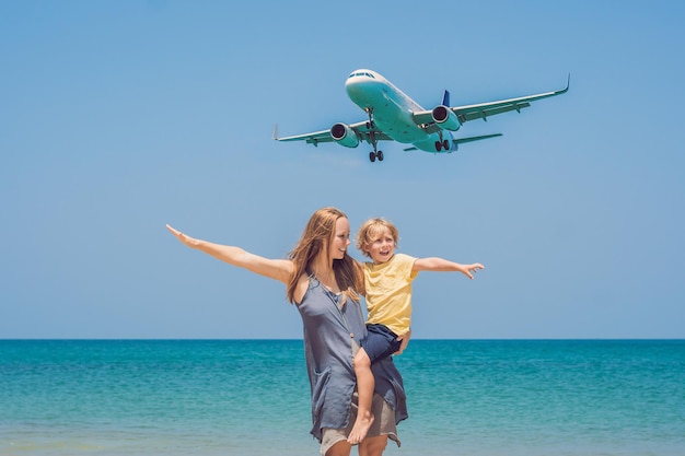 Madre e hijo se divierten en la playa mirando los aviones que aterrizan. Viajar en avión con concepto de niños.