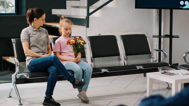 Madre e hijo esperando en la recepción del hospital, sentados en una silla para reunirse con un anciano en silla de ruedas. Personas en la sala de espera preparándose para hablar con pacientes mayores, clínica de salud.