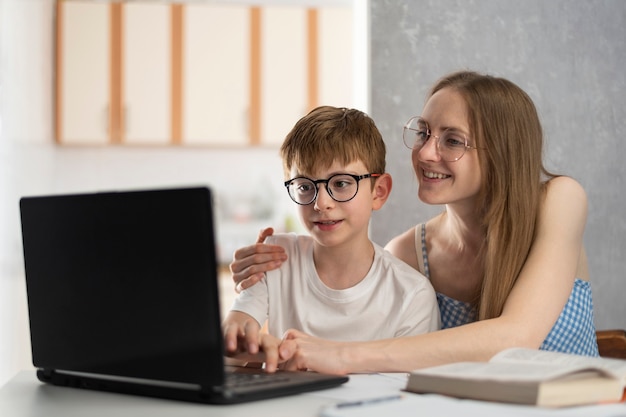 Madre e hijo están haciendo los deberes en la computadora. La hermana ayuda a su hermano con las lecciones. El tutor explica el tema al niño.