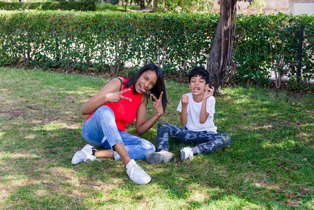 Foto madre e hijo haciendo caras mientras posan juntos sentados en la hierba en el parque