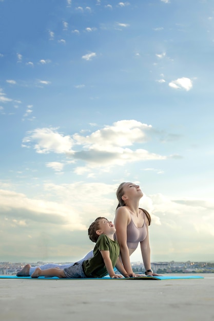 Madre e hijo haciendo ejercicio en el balcón en el fondo de una ciudad durante el amanecer o el atardecer, concepto de un estilo de vida saludable.