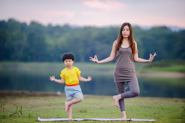 Madre e hijo haciendo ejercicios de yoga en el césped del parque antes del atardecer en verano.