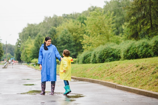 Madre e hijo jugando bajo la lluvia, con botas e impermeables