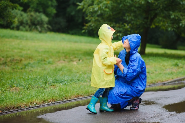 Foto madre e hijo jugando bajo la lluvia, con botas e impermeables