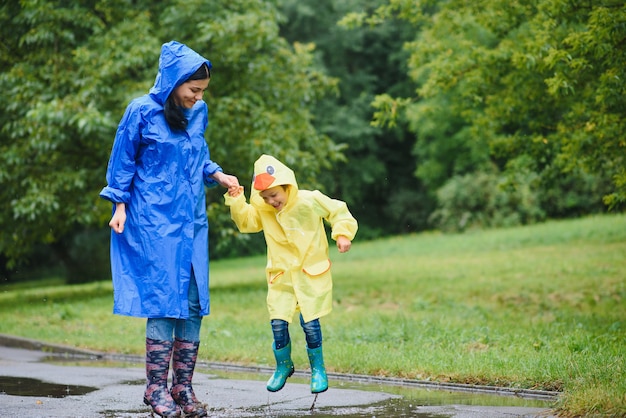 Madre e hijo jugando bajo la lluvia, con botas e impermeables