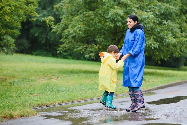 Madre e hijo jugando bajo la lluvia, con botas e impermeables