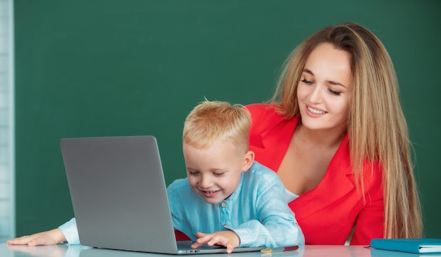 Madre e hijo juntos usando computadora portátil maestra explica la lección a niño de escuela primaria