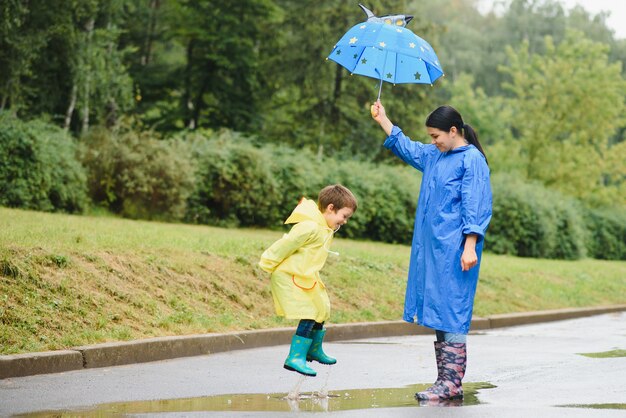 Madre e hijo, niño, jugando bajo la lluvia, con botas e impermeables.