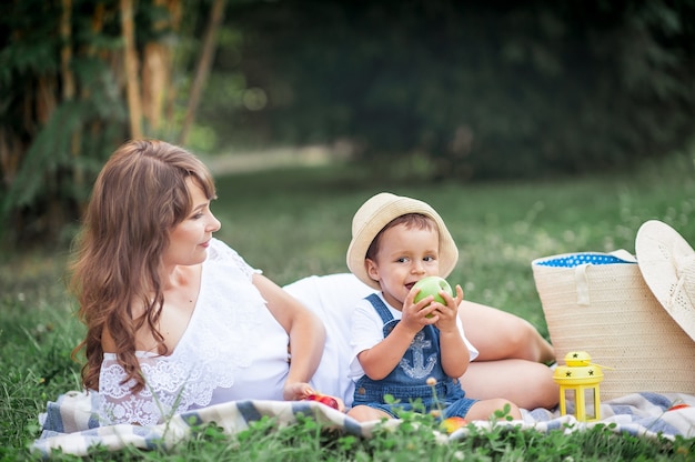 Madre e hijo pequeño jugaron en la hierba. Familia feliz camina en el parque. Mamá e hijo comiendo fruta. Picnic. Verano.