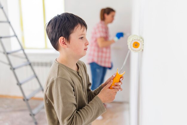 Madre e hijo pintan la pared con pintura usando rodillo y pincel