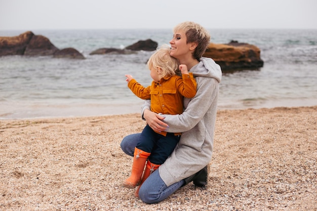 Madre e hijo sentados en la playa jugando en otoño