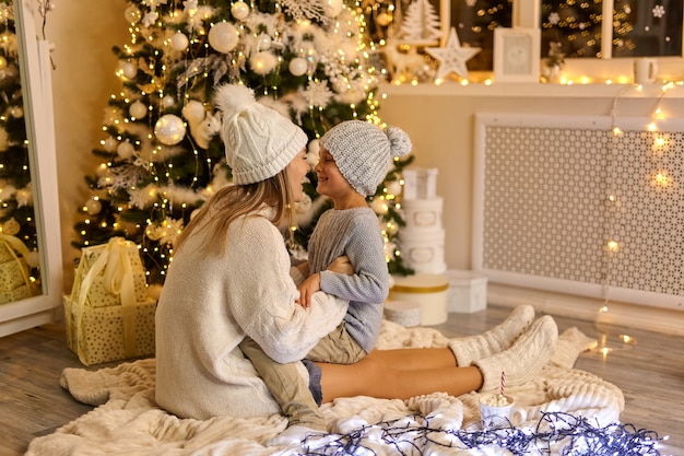 Madre e hijo en sombreros tejidos cerca del brillante árbol de Navidad