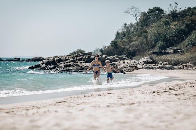 Madre e hijo en traje de baño corriendo juntos en la cama. Mamá toma la mano de su hijo. Concepto de vacaciones de verano en el mar. Phuket. Tailandia