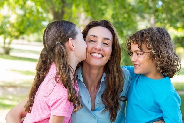 madre e hijos sonriendo y besándose en un parque