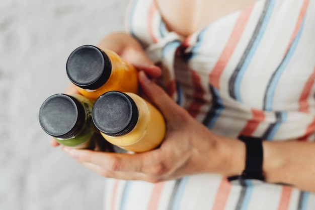 Madre embarazada sosteniendo 3 botellas de jugo de frutas y verduras prensado en frío casero