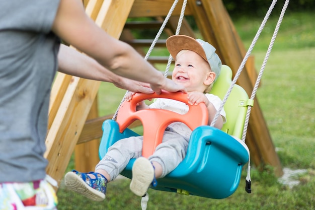 Madre empujando a su bebé niño en un columpio en el patio al aire libre