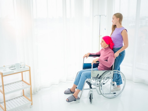 Una madre enferma de cáncer se sienta en una silla de ruedas mirando el sol de la tarde con su hija de visita en silla de ruedas en una sala de hospital