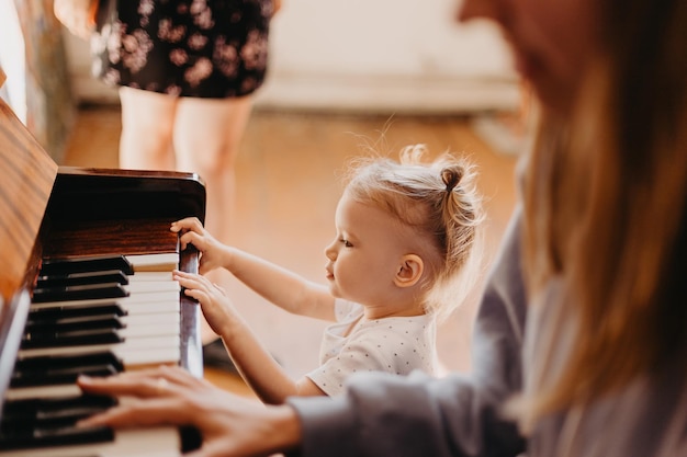 Madre enseña a una niña a tocar el piano Linda niña feliz tocando el piano en una sala de luz