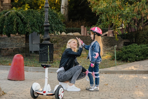 Una madre le enseña a su pequeña hija a andar en Segway en el parque durante la puesta de sol