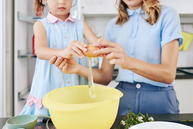 Madre enseñando a su hija cómo cascar huevos en un tazón al hacer masa para galletas