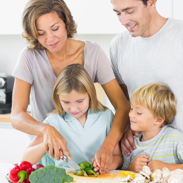 Madre enseñando a su hija a cortar verduras cuando padre e hijo están mirando