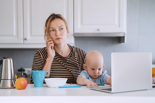 Madre equilibrando entre el trabajo y el bebé en licencia de enfermedad o maternidad Mujer respondiendo a llamadas telefónicas trabajando en una computadora portátil con el niño en su regazo Mujer sola con el bebé resuelve problemas desde casa