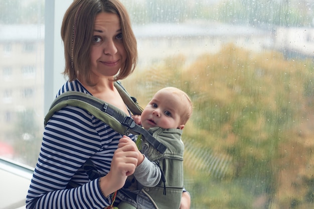 Madre con ergobaby llevar niño en casa.