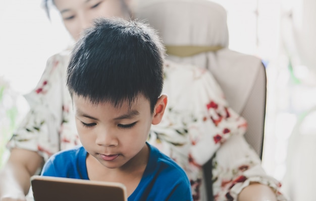 La madre está guiando a su hijo para que use la tableta de la manera correcta.