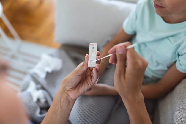 La madre le está haciendo la prueba rápida de covid-19 en casa a su hija enferma en casa. Madre realizando hisopos nasales en su hijo tomando el ejemplo para analizar si el paciente es positivo para las enfermedades infecciosas