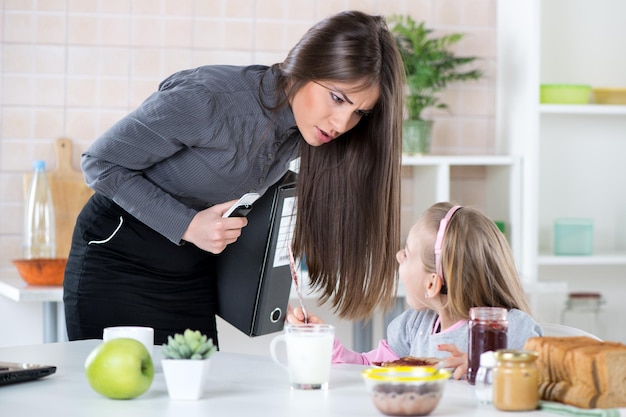 Madre con exceso de trabajo Apurando a su pequeña hija por la mañana para ir más rápido porque llega tarde al trabajo. Hija desayunando. Madre e hija se enojan entre sí por el estrés.