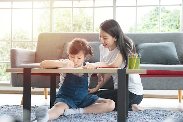 Foto madre de familia asiática y niña aprendiendo y escribiendo en el libro con lápiz haciendo la tarea.