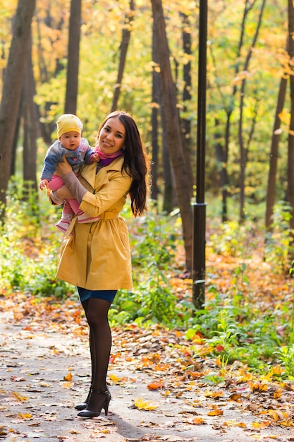La madre de familia feliz y el bebé ríen con hojas en otoño de la naturaleza.