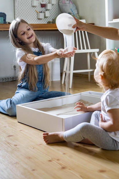Madre de familia feliz y niños jugando en casa juguetes de materiales ecológicos de desarrollo de caja de arena cinética