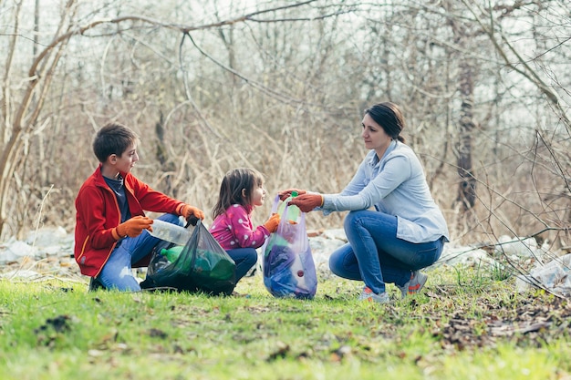 Madre de familia joven con dos niños voluntarios limpiar el parque de primavera recoger basura y botellas de plástico