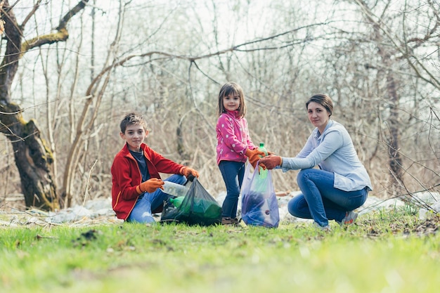 Madre de familia joven con dos niños voluntarios limpiar el parque de primavera recoger basura y botellas de plástico