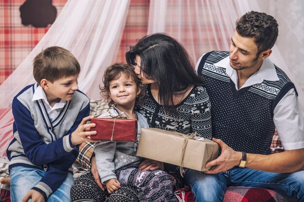 La madre de la familia, el padre y los hijos se dan regalos en la decoración de invierno de su hogar.