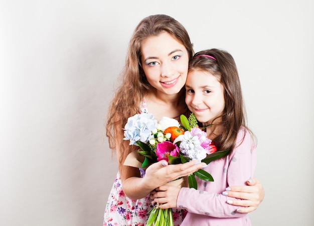 La madre feliz abraza a su hija y sostiene un ramo de flores.