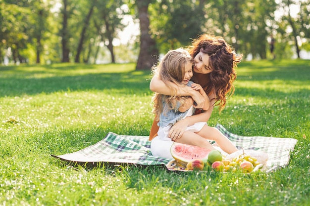 Madre feliz abrazando a su hijo mientras se sienta en la manta en el parque