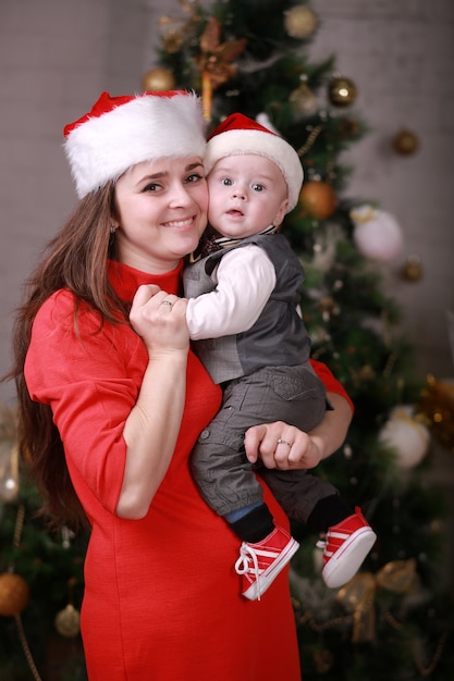 Madre feliz atractiva joven en el sombrero de santa pasar un buen rato con su hijo en casa cerca del árbol de Navidad. Familia, felicidad, vacaciones, concepto de año nuevo