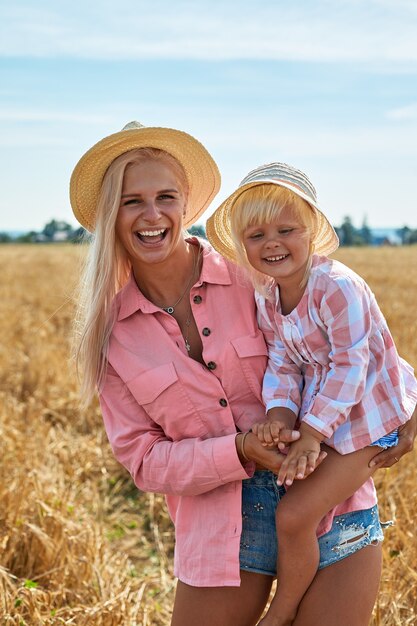 Madre feliz con bebé sonriendo en un campo de trigo en la luz del sol