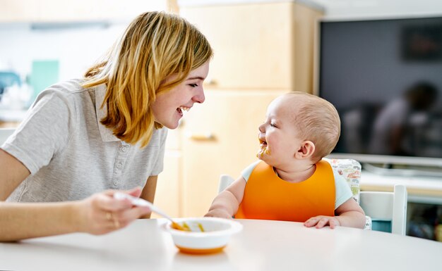 Madre feliz y bebé sonriendo durante la comida