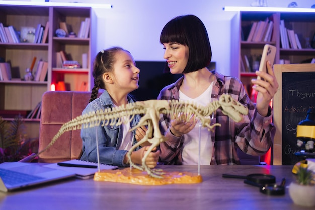 Una madre feliz examina el esqueleto de un dinosaurio con una hija linda y inteligente.