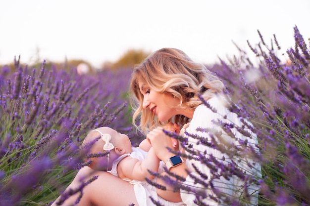 Madre feliz con una hija bonita con antecedentes de lavanda. Hermosa mujer y lindo bebé sentado en m